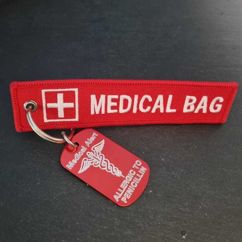 K&ouml;nnte beinhalten: Roter medizinischer Schl&uuml;sselanh&auml;nger mit einem wei&szlig;en Kreuz und dem Text "MEDICAL BAG". Der Schl&uuml;sselanh&auml;nger hat auch ein rotes Schild mit einem medizinischen Symbol und dem Text "Medical Alert" und "ALLERGIC TO PENICILLIN".