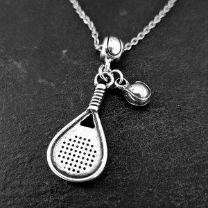 May include: A silver necklace with a charm of a paddle and a ball, representing the sport of paddle tennis.