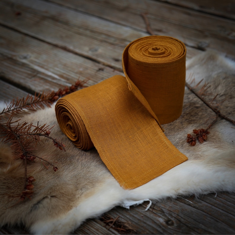 May include: A roll of mustard yellow fabric ribbon, wrapped around a similar roll of fabric. The fabric has a linen texture.