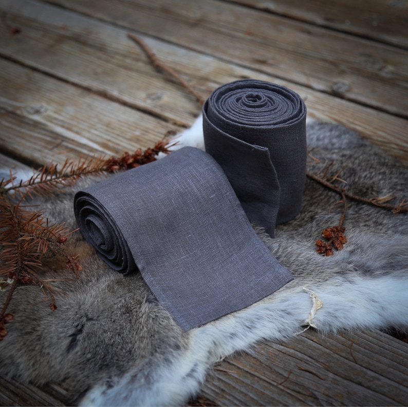 May include: Two gray fabric rolls, one larger than the other, are lying on a gray and white fur surface. The rolls are made of a soft, textured fabric.