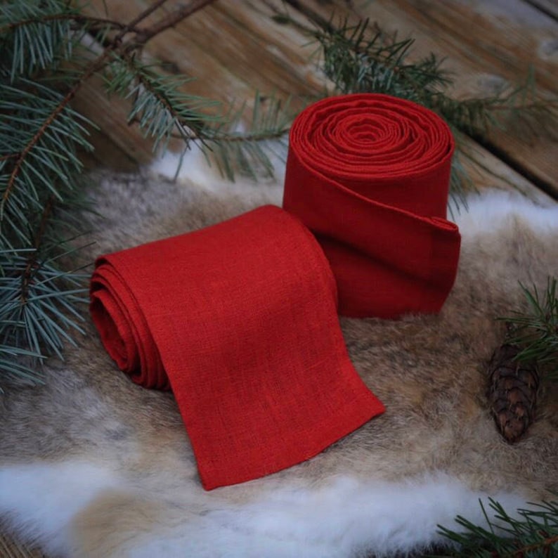 May include: Two rolls of red linen fabric, one unrolled and one rolled up. The fabric is a deep red color and has a natural linen texture.