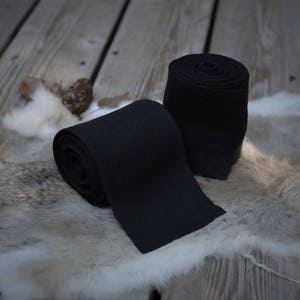 May include: Two rolls of black fabric, likely for wrapping or binding, are displayed on a white fur surface. The fabric is tightly rolled and appears to be made of a soft, natural material.