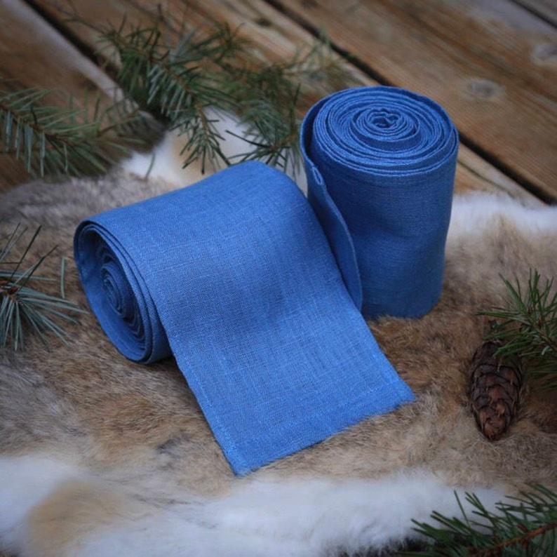 May include: Two rolls of blue linen fabric, one rolled up and the other unrolled, lying on a brown fur surface.