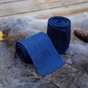May include: Two rolls of dark blue linen fabric. The fabric is rolled up and tied with a knot. The fabric is on a gray fur surface.