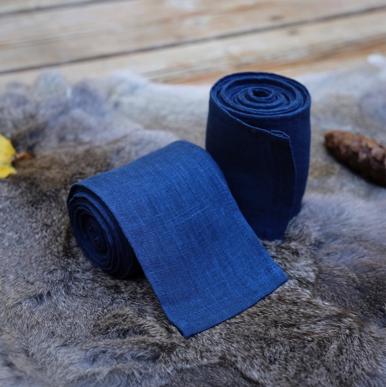 May include: Two rolls of dark blue linen fabric. The fabric is rolled up and tied with a knot. The fabric is on a gray fur surface.