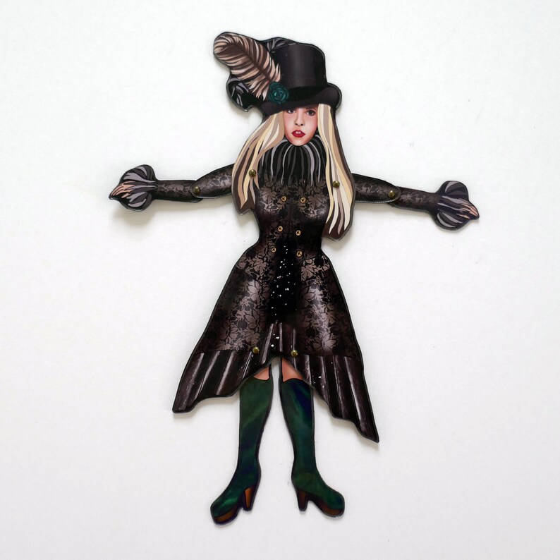 May include: A decorative cutout of a woman in a black Victorian-style dress and top hat. The dress features a floral lace pattern and gold-colored studs. The woman has blonde hair, red lips, and is wearing green boots.