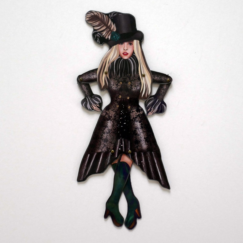 May include: A wooden cutout of a woman in a black Victorian-style outfit. She wears a top hat with a feather, a ruffled collar, and a long coat with floral detailing. Her boots are dark green.