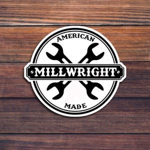 Op de afbeelding: Een witte ronde sticker met een zwarte rand en de tekst "AMERICAN MILLWRIGHT MADE" in een banner. Twee zwarte sleutelvormen zijn in het midden gekruist.