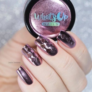 May include: Pink metallic nail polish with a heart design. The jar of polish has the text "What's Up Nails" on the label.
