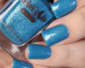 Op de afbeelding: Een flesje nagellak van het merk What's Up Nails in een levendige, glinsterende blauwgroene kleur. Het flesje wordt vastgehouden naast nagels die in dezelfde tint zijn gelakt. Het flesje bevat 11 ml nagellak.