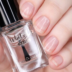 May include: A clear glass bottle of What's Up Nails nail polish with a black cap and a black brush. The bottle is labeled with the brand name and the volume, 11mL (0.37 fl oz).