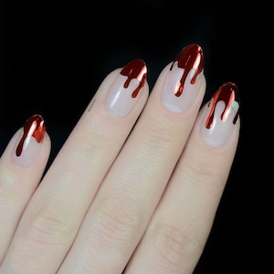 May include: Close-up of a hand with red and gold nail polish. The nails are painted with a dripping effect, resembling blood.