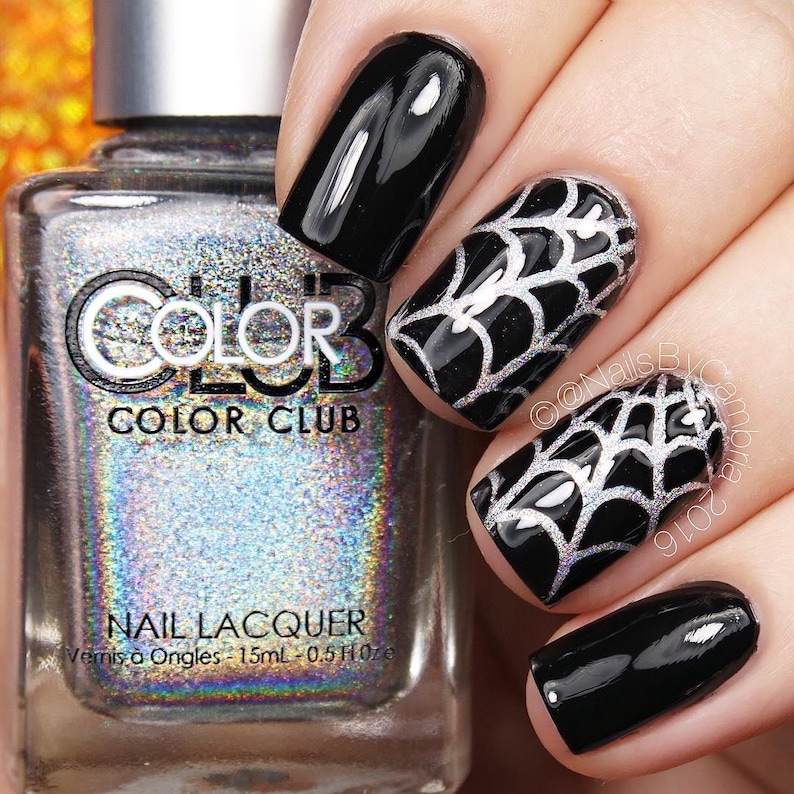May include: Black nail polish with silver spiderweb designs. The nail polish bottle is silver with a holographic finish and the text "COLOR CLUB" on the label.