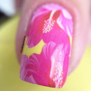 Puede incluir: Primer plano de un dise&ntilde;o de u&ntilde;as floral rosa y amarillo. El dise&ntilde;o presenta una flor de hibisco con detalles blancos.