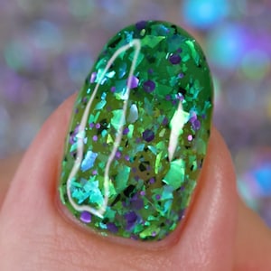 May include: Close-up of a green nail polish with iridescent glitter. The glitter is a mix of green, blue, and purple.