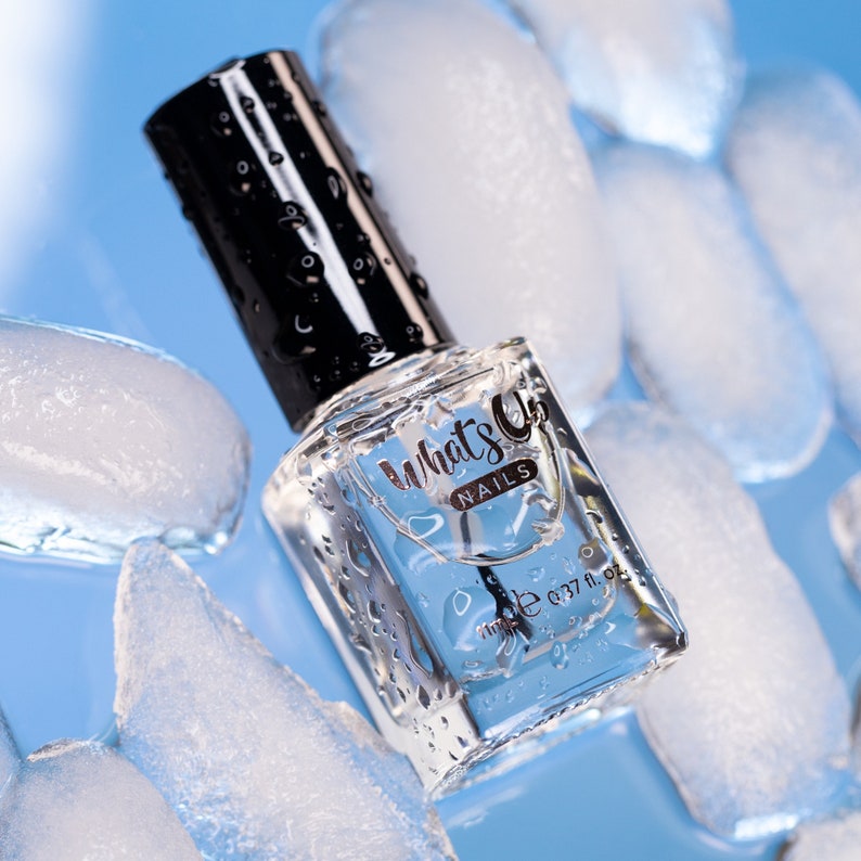 May include: A clear glass bottle of nail polish with a black cap. The bottle is surrounded by ice cubes and the label reads "What's Up Nails" with a small bottle size of 0.37 fl oz.