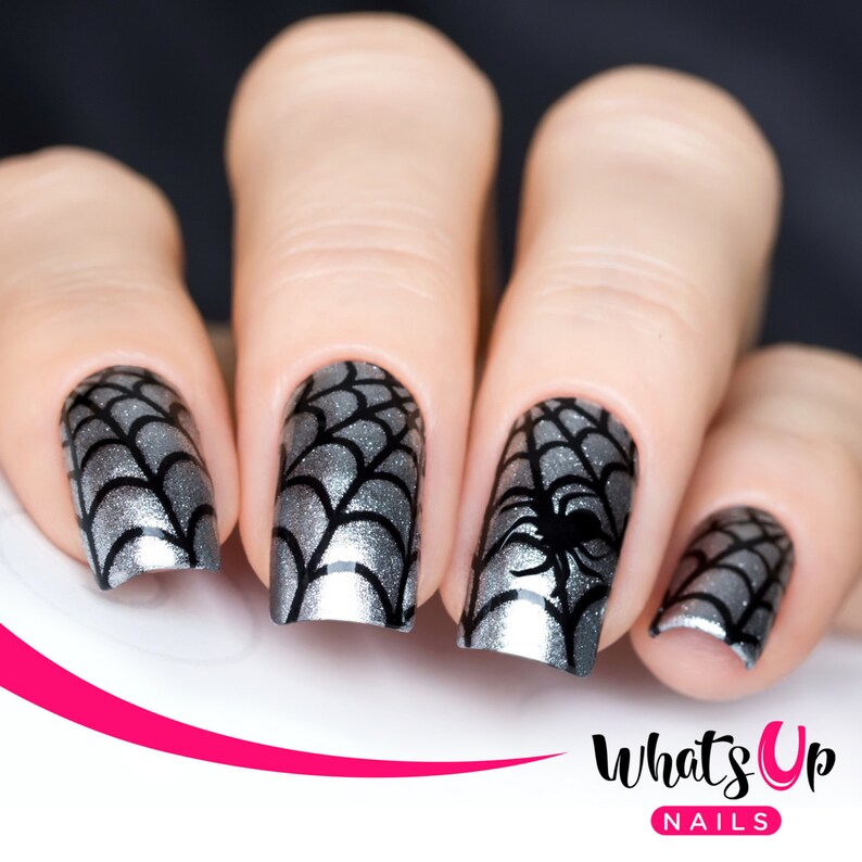 May include: Close-up of four fingernails with a silver and black spiderweb design. The design features a black spider on one nail. The nails are painted with a silver glitter polish.