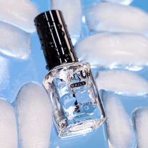 May include: A clear glass bottle of nail polish with a black cap. The bottle is surrounded by ice cubes and has the text "What's Up Nails" on the label. The bottle contains 0.37 fl. oz. of nail polish.