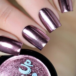 May include: Close-up of fingernails painted with a metallic rose gold nail polish. The polish has a high shine and a smooth finish. The nail polish is in a small jar with a black lid.
