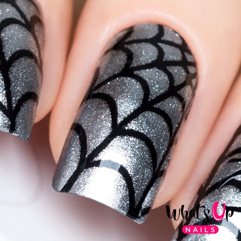 May include: Close-up of fingernails with a silver glitter base and black spiderweb design. The nails are short and square shaped. "What's Up Nails" is written in white letters on a pink background.