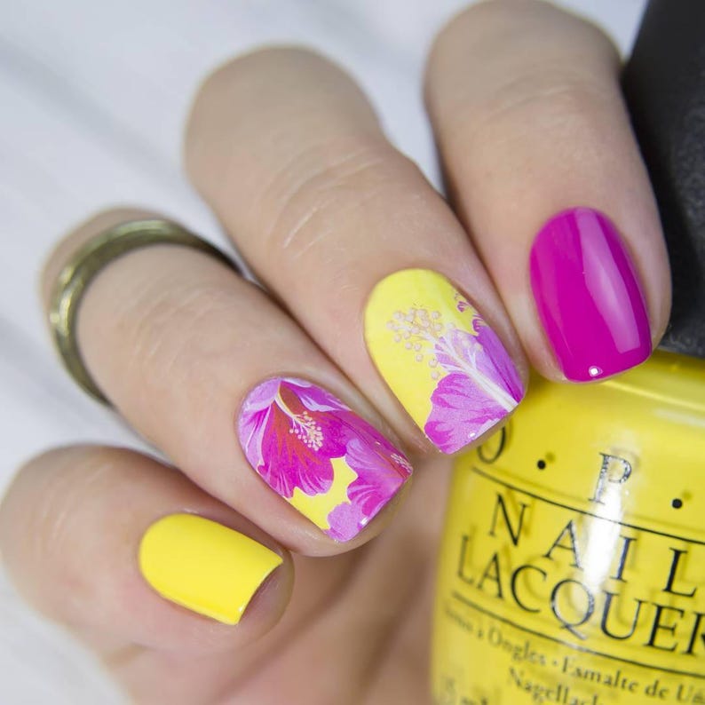 Puede incluir: Primer plano de una mano con esmalte de u&ntilde;as amarillo y rosa. Las u&ntilde;as est&aacute;n decoradas con dise&ntilde;os florales. Se puede ver una botella de esmalte de u&ntilde;as amarillo con el texto "OPI Nail Lacquer" en el fondo.