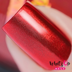 Puede incluir: Primer plano de un esmalte de uñas rojo con acabado metálico. El esmalte tiene un brillo fino y se aplica a una uña.