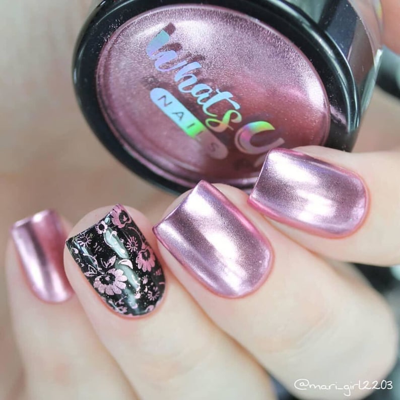 May include: Pink metallic nail polish with a floral design on one nail. The jar of nail polish has the text "What's Up Nails" on the label.