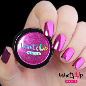 K&ouml;nnte beinhalten: Ein kleines Glas mit rosa metallischem Nagelpulver mit dem Text "What's Up Nails" auf dem Etikett. Eine Hand ist mit mehreren N&auml;geln zu sehen, die mit dem rosa metallischen Nagelpulver lackiert sind.
