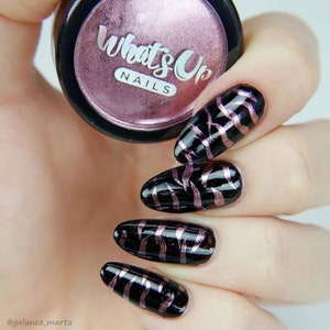 May include: Close-up of five fingernails with black nail polish and a pink and gold metallic design. The nails are long and oval shaped. The image also shows a small jar of nail polish with the text "What's Up Nails" on the label.