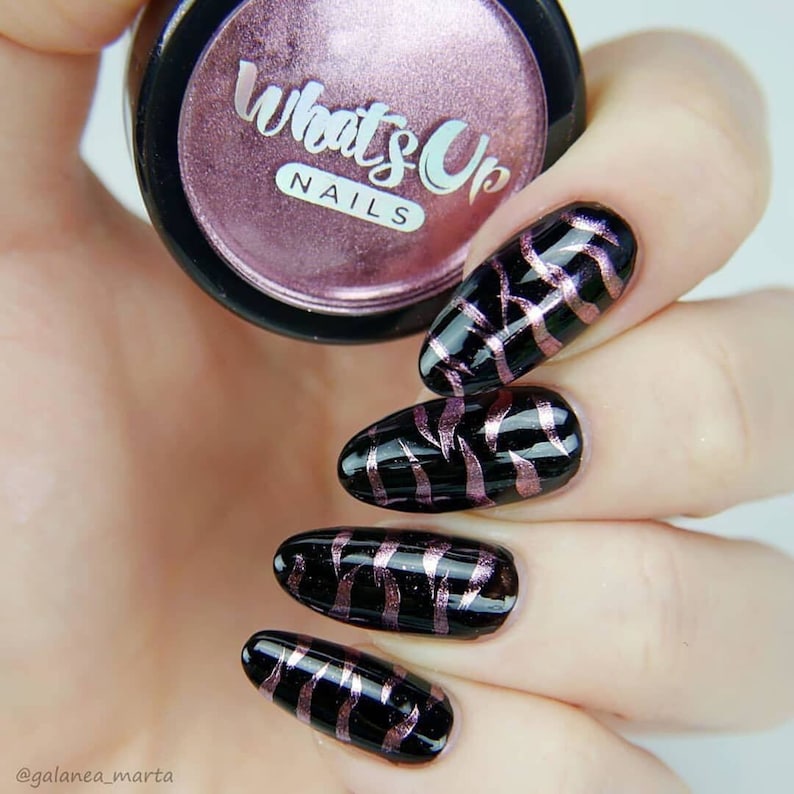 May include: Close-up of five fingernails with black nail polish and a pink and gold metallic design. The nails are long and oval shaped. The image also shows a small jar of nail polish with the text "What's Up Nails" on the label.