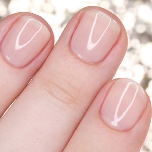 Puede incluir: Primer plano de tres uñas con un esmalte de uñas rosa claro. Las uñas son lisas y brillantes.
