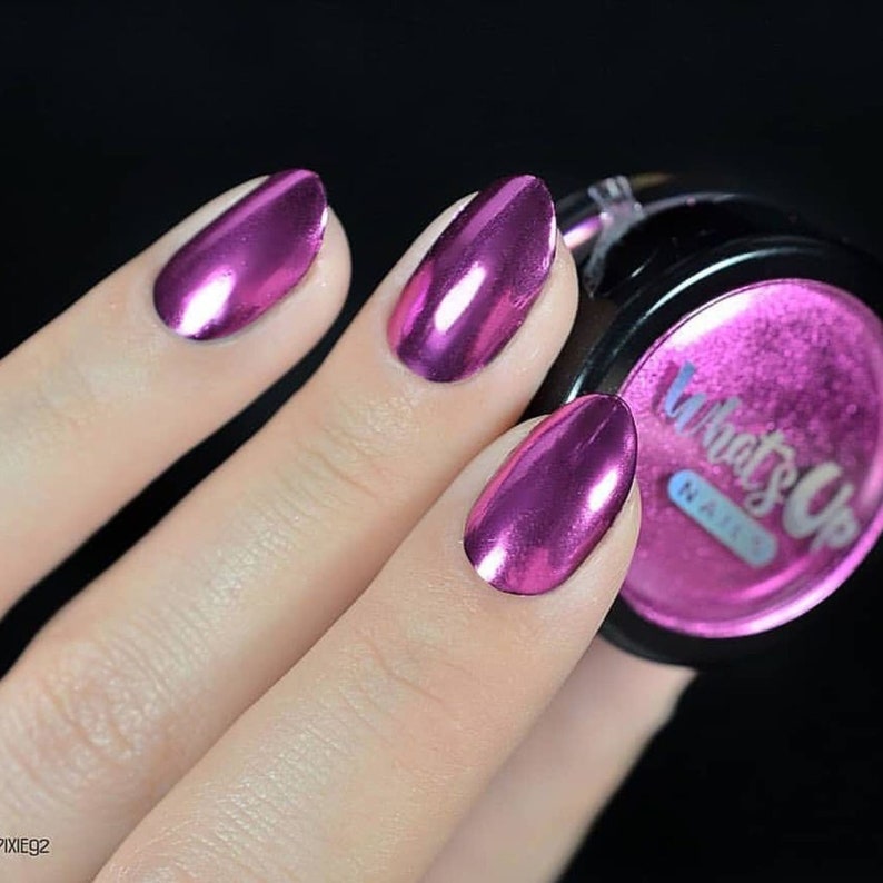 K&ouml;nnte beinhalten: Nahaufnahme einer Hand mit pinkfarbenem Metallic-Nagellack. Die N&auml;gel sind oval geformt und haben einen hochgl&auml;nzenden Finish. Im Hintergrund ist ein kleines Glas mit pinkfarbenem Metallic-Nagellack zu sehen. Das Glas hat einen schwarzen Deckel und der Text "What's Up Nails" ist auf dem Etikett aufgedruckt.