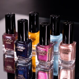 May include: A collection of six nail polish bottles with black caps and gold lettering. The bottles contain different colors of nail polish, including purple, gold, blue, and pink. The bottles are labeled "What's Up Nails" and have a volume of 0.37 fl oz.