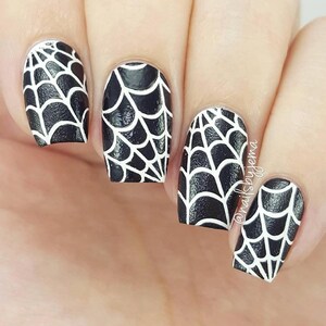 May include: Close-up of four fingernails painted black with white spiderweb designs. The nails are short and square shaped. The design is intricate and detailed, with thin white lines creating a web-like pattern.