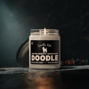 Puede incluir: Una vela de cera de soja blanca en un tarro de vidrio con una etiqueta negra que dice "C" Smells like DATE NIGHT WITH MY DOODLE 100% SOY WAX CANDLE 50-60 HRS BURN TIME". La etiqueta también presenta una silueta de un perro doodle.