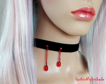 May include: A black velvet choker necklace with red chain and teardrop earrings. The earrings and the choker have red accents. The image shows a close-up of the neck and part of the face.