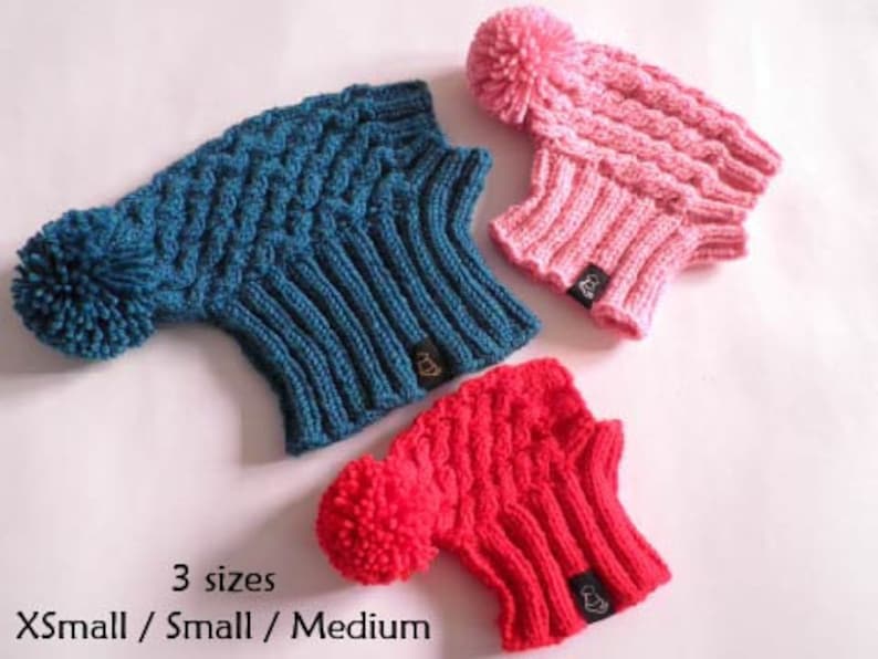 May include: Three knitted hats with pom-poms in blue, pink, and red. The hats are available in three sizes: X-Small, Small, and Medium.