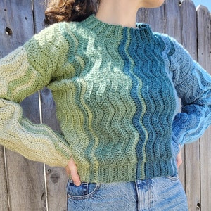 May include: A green and blue ombre crochet sweater with a wavy pattern.