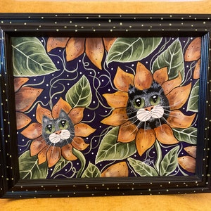 May include: Framed painting of two black cats with green eyes peeking out of sunflowers on a purple background with white dots.