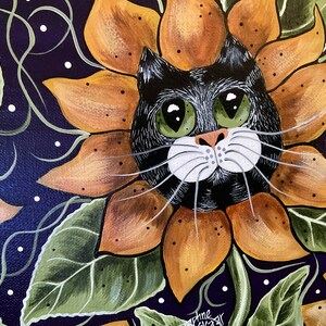 May include: A black cat with green eyes peeks out from a sunflower with orange and brown petals. The background is a dark purple with white dots and green leaves.