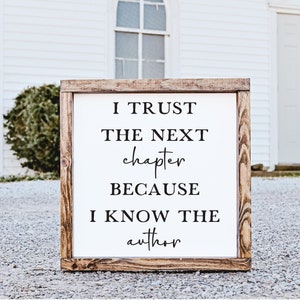 May include: A wooden sign with the text "I trust the next chapter because I know the author" in black lettering on a white background.