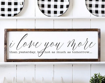 May include: A white wooden sign with a brown frame, featuring the text "i love you more than yesterday, but not as much as tomorrow..."
