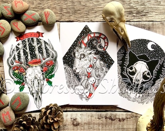 Könnte beinhalten: Drei Kunstdrucke mit detaillierten Schwarz-Weiß-Illustrationen. Einer zeigt einen Hirschschädel mit Geweih und Pilzen, ein weiterer einen Widder mit Glocken und der letzte einen Katzenschädel unter einem Mond. Runen und ein Vogelschädel sind ebenfalls vorhanden.