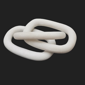 Puede incluir: Una escultura decorativa blanca entrelazada en forma de cadena. La escultura está hecha de un material sólido y liso y presenta un diseño en bucle. La pieza está colocada sobre un fondo oscuro, resaltando su forma y textura. Esta obra de arte moderna es adecuada para la decoración del hogar.