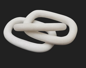 May include: A white, interlocking decorative chain sculpture. The sculpture is made of a solid, smooth material and features a looped design. The piece is set against a dark background, highlighting its form and texture. This modern art piece is suitable for home decor.