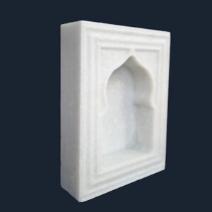 May include: A white marble wall niche with an arched top and rectangular frame. The niche has a recessed interior and is carved with subtle details. The overall design is simple and elegant, suitable for displaying small objects.
