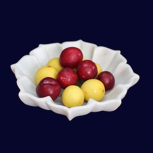 Może przedstawiać: Biała marmurowa miska z karbowanym brzegiem, wypełniona czerwonymi i żółtymi śliwkami.