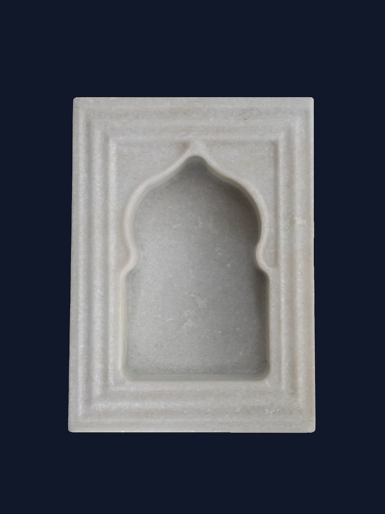 May include: A white marble wall niche with an arched top and rectangular frame. The niche has a recessed interior and is designed with a layered, textured border. The background is a dark blue.