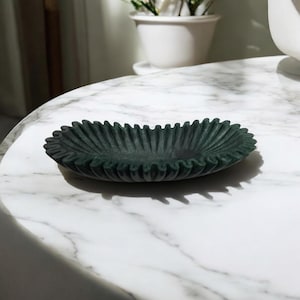 May include: A dark green, oval-shaped decorative bowl with a ruffled edge. The bowl is made of a textured material and has a unique, organic shape.