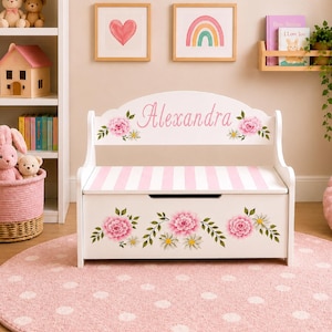 May include: A white wooden toy chest bench with a hinged lid, featuring a pink and white striped seat. The backrest is personalized with the name Alexandra in pink script, surrounded by floral illustrations of pink peonies and green leaves.